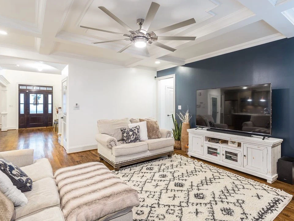 Living room with coffered ceiling, built-in white cabinetry and a navy feature wall
